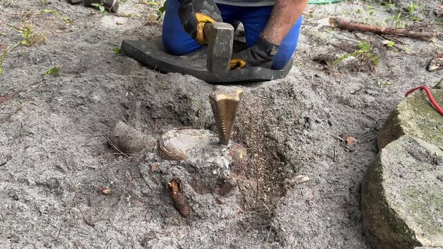 Man Splitting Tree Stump with Wedge and Hammer in Backyard