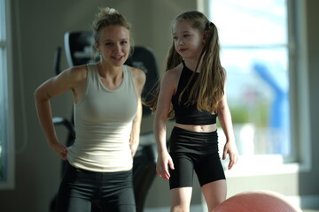 Fototapeta premium Mother and young daughter stretch and exercise together on a mat in a bright gym, sharing a healthy active lifestyle.