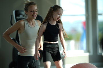 Fototapeta premium Mother and young daughter stretch and exercise together on a mat in a bright gym, sharing a healthy active lifestyle.