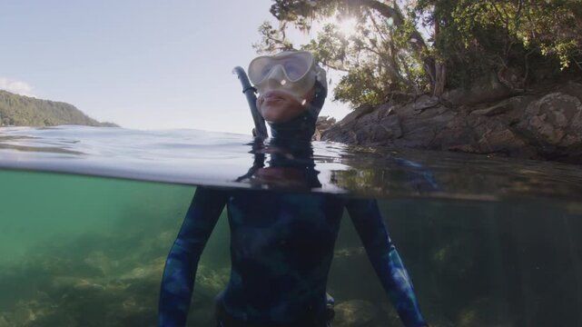 Freediving in Brazil, underwater camera. Woman freediver in the blue wetsuit swims in the sea near the island of Ilha Grande in Brazil and looks around