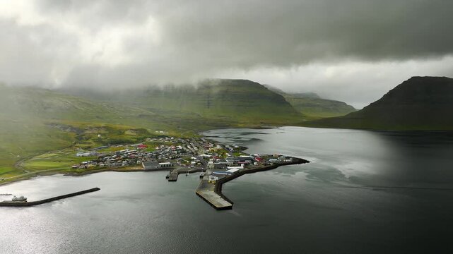 Aerial reveal of coastal village under rolling mist across mountain ridge