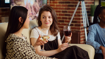 BFFs talking on couch, drinking wine and champagne at friends social reunion and catching up with...