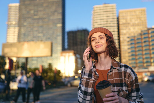 Woman with coffee on phone in city street, smile and relaxed beanie style captured in golden hour glow with candid authenticity, mindful living and emotional storytelling urban lifestyle scene.