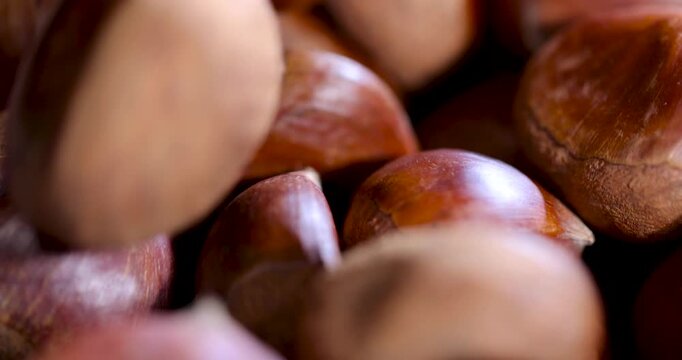 Smooth brown chestnuts, the chestnut fruit harvest is collected in a small bowl standing on a dark wooden surface with cracks.
