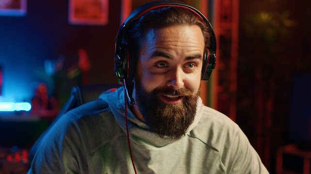 Esports player playing videogames in front of subscribers during livestream, providing winning strategy tips during gameplay, close-up on professional gamer streaming game in neon lit studio.