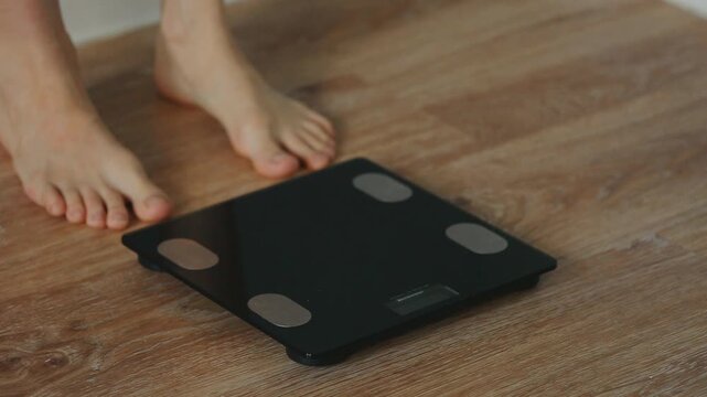 Woman pulls the toe of the foot, stretching exercise for her legs with bare feet when stepping on digital floor scales, weighing, checking at home. Closeup