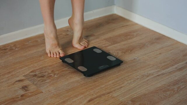 Woman pulls the toe of the foot, stretching exercise for her legs with bare feet when stepping on digital floor scales, weighing, checking at home 
