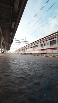 Commuter electric train arriving at the station platform under a clear sky with a low angle static wide shot