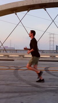 Athletic Man working out by jogging across the 6th Street Bridge over the LA River near downtown Los Angeles at dawn. Vertical video.