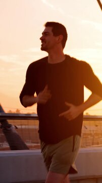 Athletic Man working out by jogging across the 6th Street Bridge over the LA River near downtown Los Angeles at dawn. Vertical video.