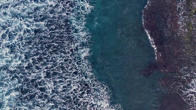 Aerial looking down at waves on a black sand beach in Bali Indonesia.