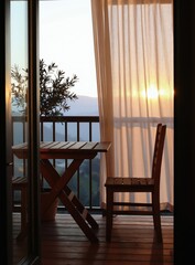 Obraz premium Wooden balcony furniture with a tree sits near railings. Soft curtains blow gently in warm sunrise light overlooking misty hills. Peaceful morning view.