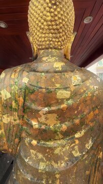 A golden Buddha statue adorned with gold leaf, a common practice in Buddhist temples in The Grand Palace, Bangkok, Thailand, symbolizing reverence and merit-making.