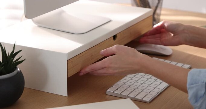 Woman opening drawer of under monitor riser at wooden desk indoors, closeup