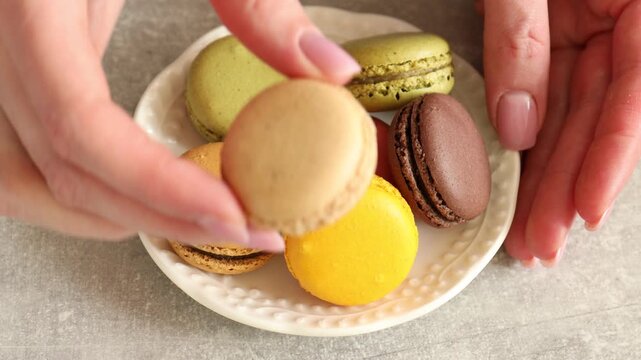 Woman showing colorful macarons at light grey table, closeup