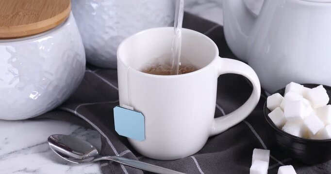 Making tea. Pouring hot water into cup with teabag at white marble table, closeup