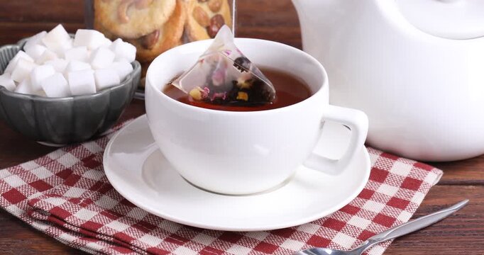 Making tea. Woman putting teabag into cup with hot water and adding sugar at wooden table, closeup
