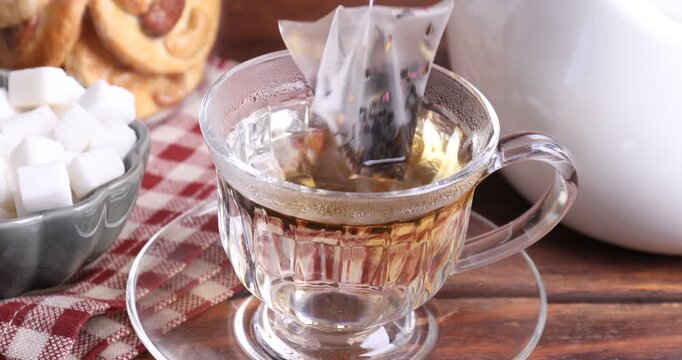 Making tea. Putting teabag into cup with hot water at wooden table, closeup
