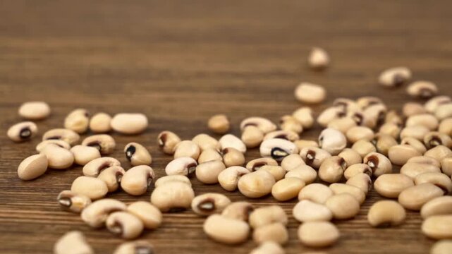 Black eyed beans spilling across a natural brown wooden tabletop background close up