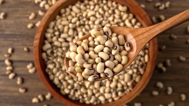 Wooden spoon gently scooping dry black eyed beans from a full wooden bowl on a textured dark background