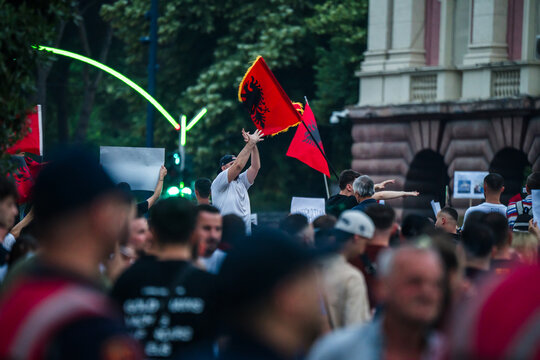 Tirane, Albania - 03 June 2026: View of a crowd of protesters holding Albanian flags and signs in front of a historic building during a demonstration.