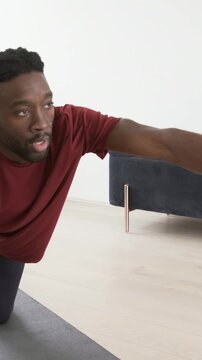 Vertical video: Reaching right arm, man in maroon shirt moving into quadruped on mat, for exercise
