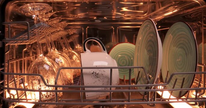 Close-up view inside dishwasher with clean glassware plates and cups after washing cycle finished.
