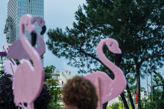 Tirana, Albania - 03 June 2026: View of pink flamingo cutouts held by people during a public gathering in front of modern buildings and green trees.