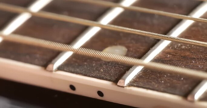 Close up of acoustic guitar fretboard with strings and fret markers showing dust detail.