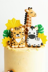 Obraz premium Safari themed birthday cake features tiger, zebra, and giraffe cookies. Yellow frosting adorns cake with edible jungle leaves. Perfect for kids party celebration.