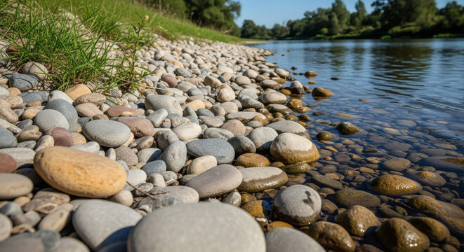 Close-up of smooth colorful river stones and pebbles along a serene riverbank with green grass and blue water