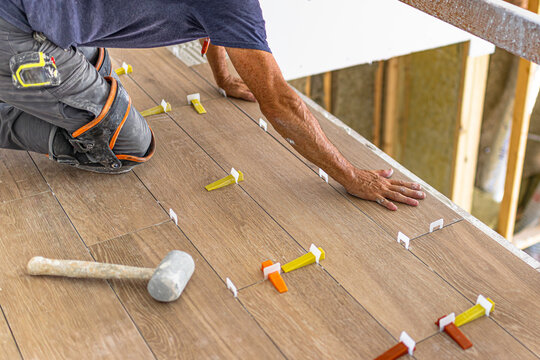 Close up view of tiler installing wood look ceramic floor tiles using leveling system clips and wedges on construction site