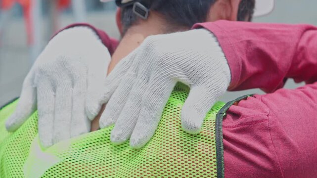 Rear view of a worker massaging a stiff neck, experiencing muscle strain during construction work.