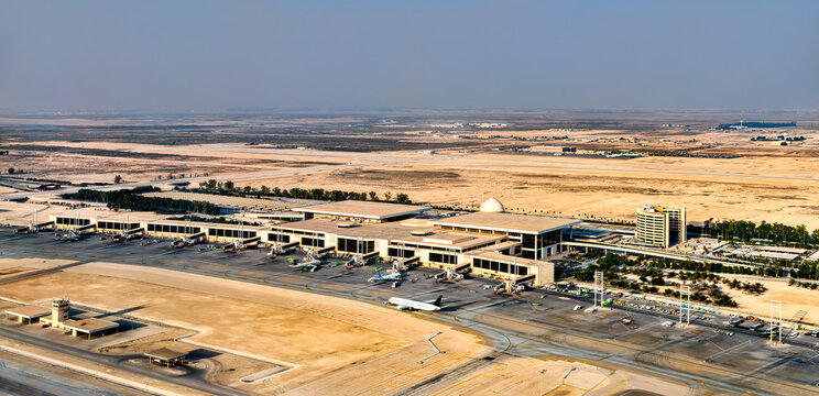 High angle view of the King Fahd International Airport terminal and tarmac in Dammam, Saudi Arabia, featuring airplanes parked at gates and the surrounding desert landscape.
