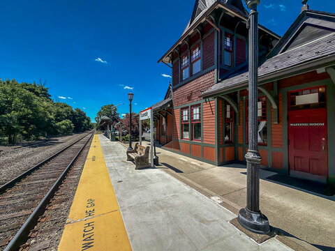 Tuxedo, NY - US -Jun 13, 2026 A historic, shingle-style train station platform under a bright blue sky, featuring a decorative tower with a weather vane and an informational poster display case.