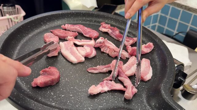 Close-up footage of fresh raw meat being placed onto a hot tabletop charcoal or gas grill at a traditional Korean barbecue restaurant. Steam and first sizzling sounds as the meat hits the grill 