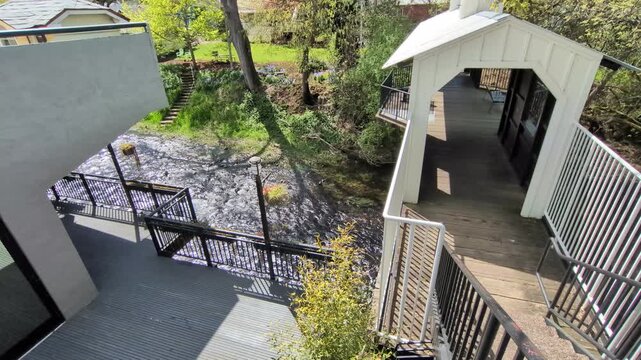 A scenic riverfront path leading to a historic covered bridge with benches and observation areas, capturing the peaceful beauty on a bright spring day.