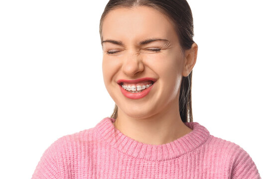 Beautiful young woman with dental braces suffering from pain on white background