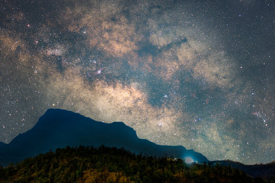 View of the Milky Way galaxy shining brightly over a dark mountain silhouette and forested hills in Dehene, Maharashtra, India.