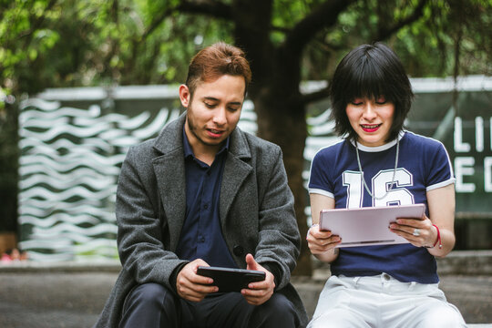 Two Young Hispanic friends playing mobile games together outdoors