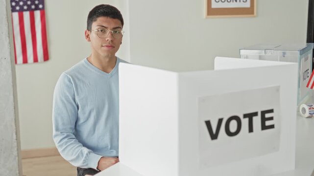 Man holding ballot in hand at voting booth inside building, smiling and raising paper; civic duty pride.