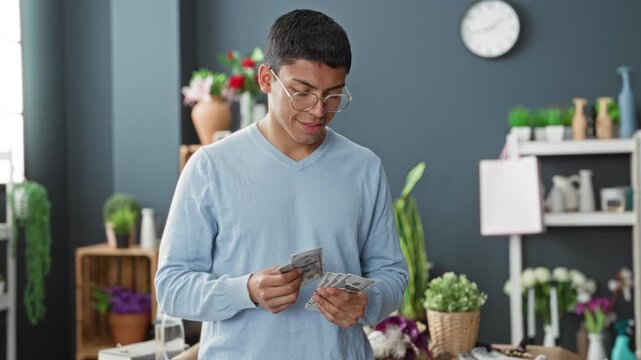 Man florist counts cash in hands amid vases, flowers and potted plants in studio, smiling while tallying dollars; quiet satisfaction.