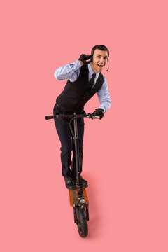Male worker in headset with kick scooter on pink background