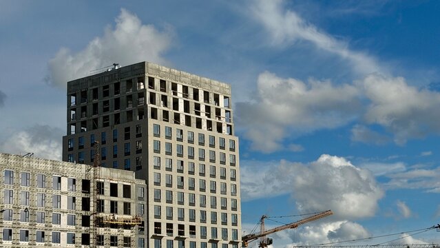 High-rise apartment tower under construction at Salaryevo Park district in Moscow by PIK. Concrete cement structure next to blue sky with white clouds. Urban development and real estate concept.