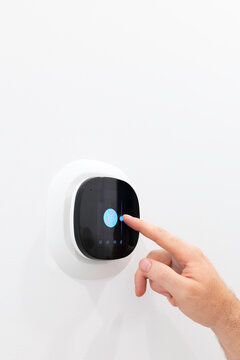 Close up view of hand touching smart digital thermostat screen on white wall to adjust temperature slider
