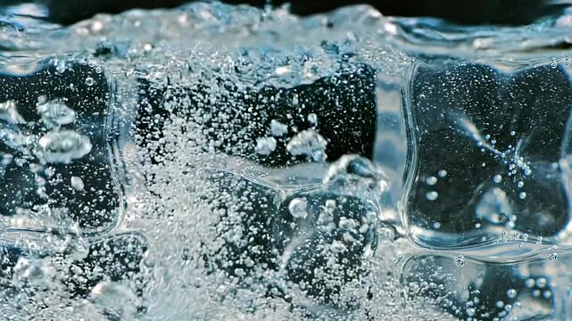 Inside-glass macro perspective between ice cubes as a fresh cube drops from above and plunges past the lens, releasing bubbles and ripples in crystal clear liquid, capturing dynamic refreshment