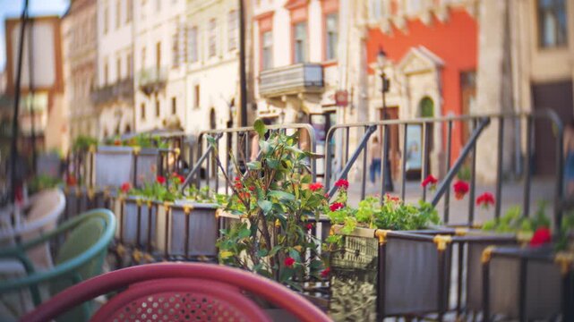 A cozy outdoor cafe terrace with red flowers in flowerpots stands in a charming European street. Cinematic look with vignette and swirled background.
