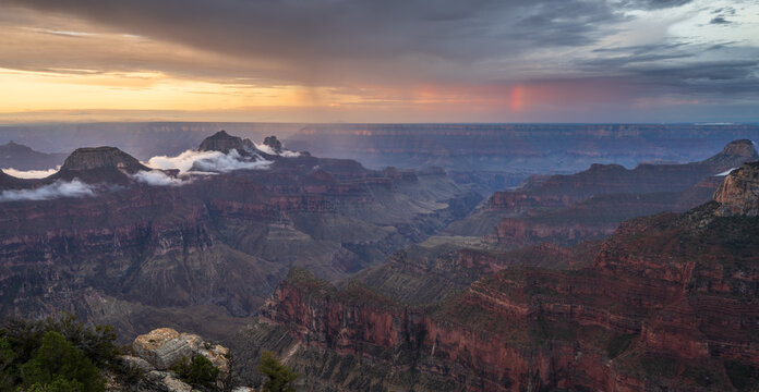 View of the Grand Canyon with mist floating between rocky cliffs under a dramatic sunset sky with a faint rainbow Coconino County, Arizona, United States.