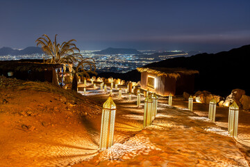 Obraz premium Traditional illuminated lanterns line a rocky path at Jabal Uhud viewpoint, offering a scenic night view of the city lights in Madinah, Saudi Arabia