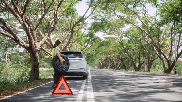 Person standing by car on roadside after tire change under trees